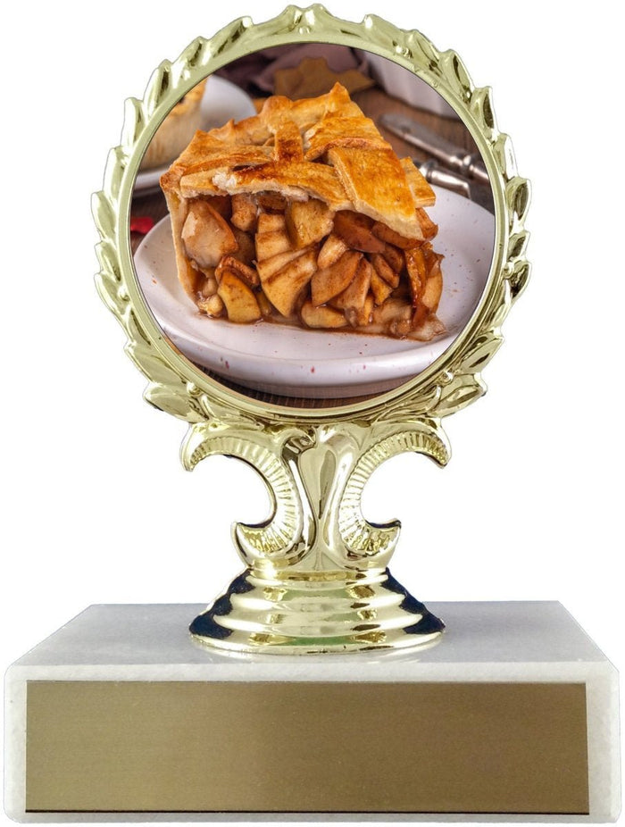 A gold trophy-style plaque holder with a round decorative frame displaying a photo of a slice of apple pie, mounted on a tiered gold pedestal over a rectangular white base with a gold front panel.