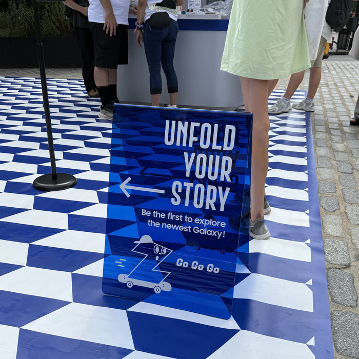 Transparent blue acrylic A-frame sign with Unfold Your Story lettering at an event.