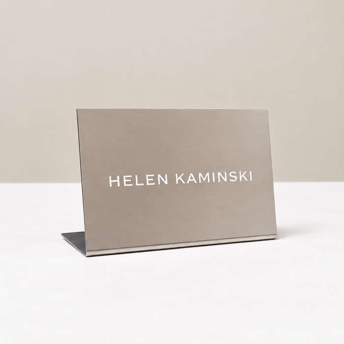 Landscape stainless steel tabletop stand with white Helen Kaminski lettering.