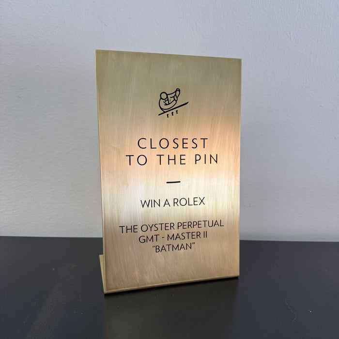 Angled view of a brass tabletop sign with Closest to the Pin prize information.