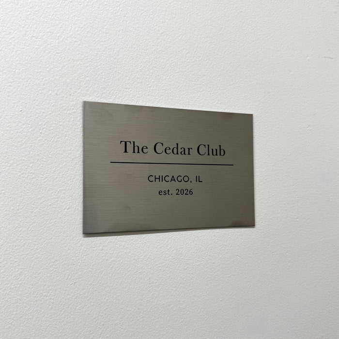 Rectangular stainless steel plaque with The Cedar Club lettering mounted on a wall.