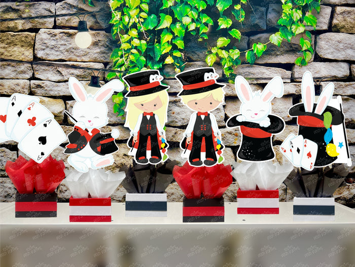 Kids birthday party magician themed centerpieces. The centerpieces feature illustrated cutouts including playing cards, a white rabbit in a tuxedo, a girl magician, a boy magician, a rabbit popping out of a top hat, and a magician's hat with a wand. Each cutout is set in a red, white, or black base filled with matching tissue paper. Receive fully assembled like pictured.