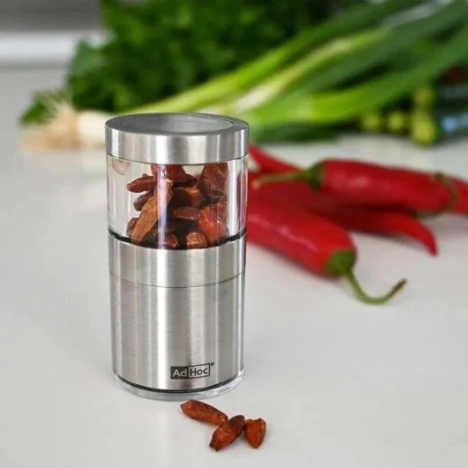 Stainless steel spice grinder with red peppers and green onions in the background