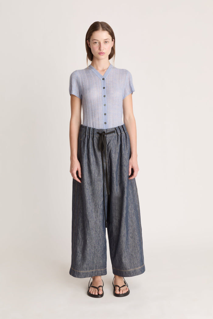 Woman wearing a light blue button-up shirt and dark blue wide-leg pants on a plain background