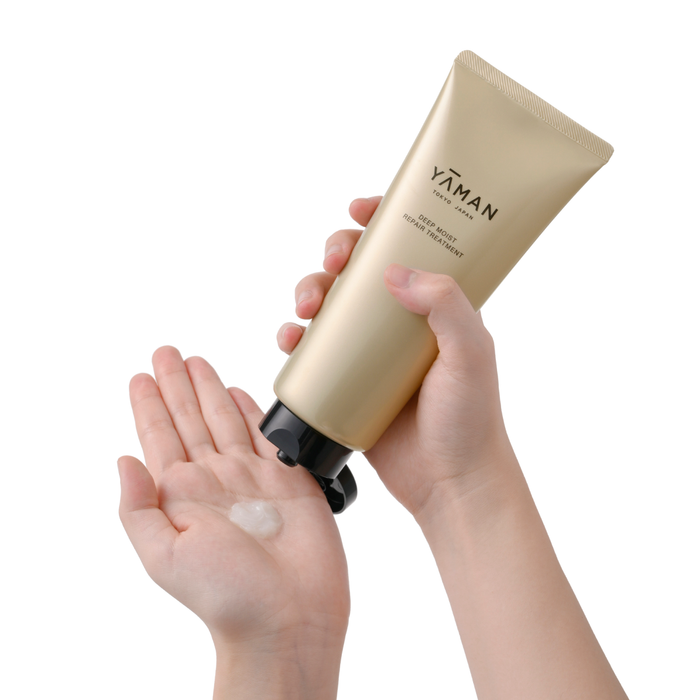Gold tube of YAMAN skincare product being held with a hand applying cream to another hand on a white background