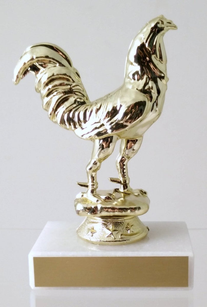 A trophy featuring a gold-colored rooster figurine mounted on a white marble base and gold engraving plate
