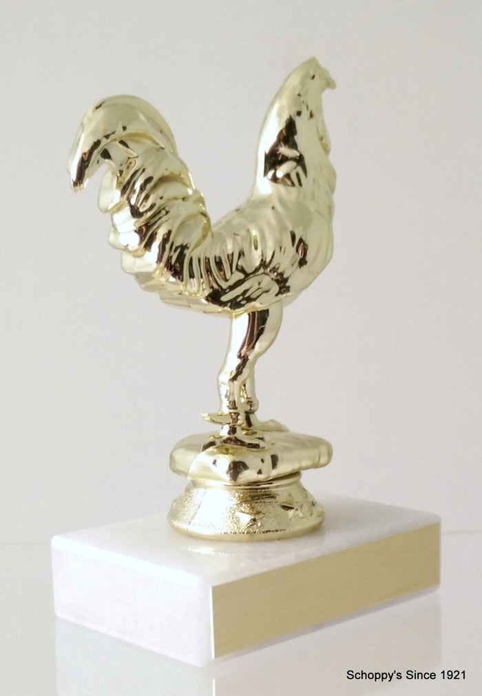 A trophy featuring a gold-colored rooster figurine mounted on a white marble base and gold engraving plate