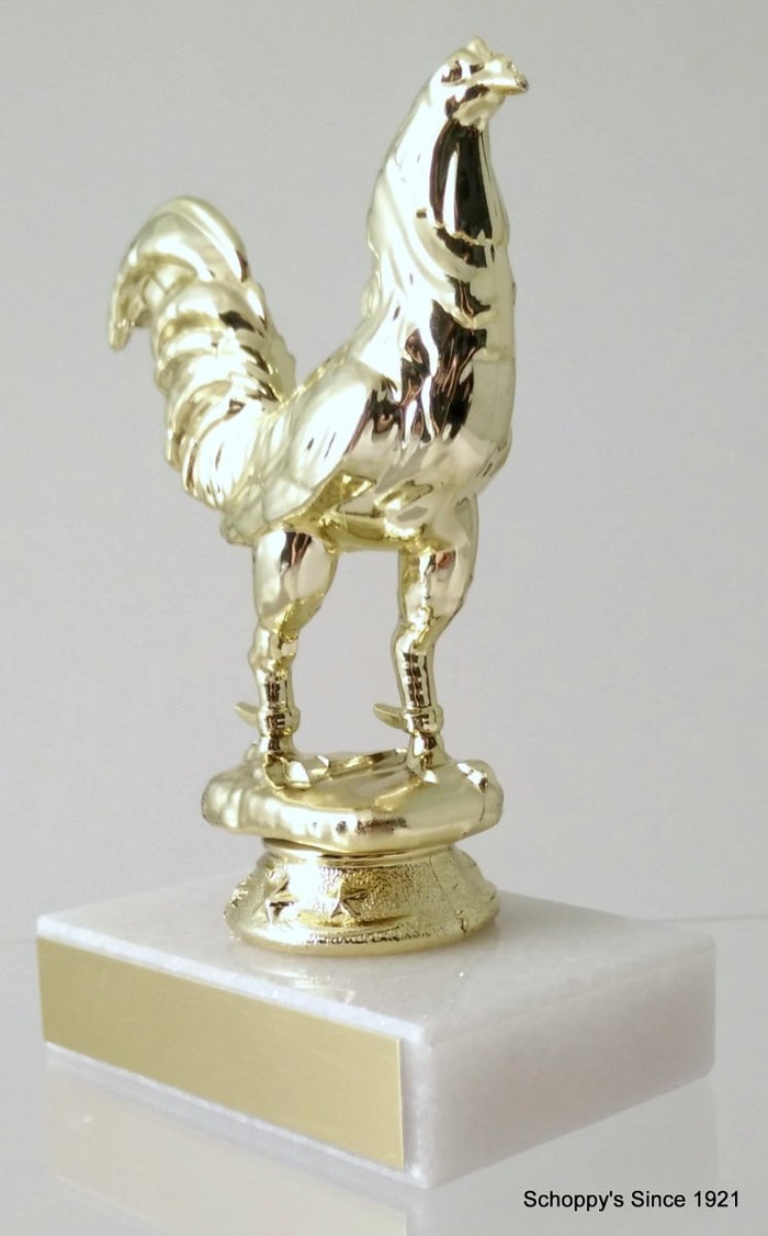 A trophy featuring a gold-colored rooster figurine mounted on a white marble base and gold engraving plate