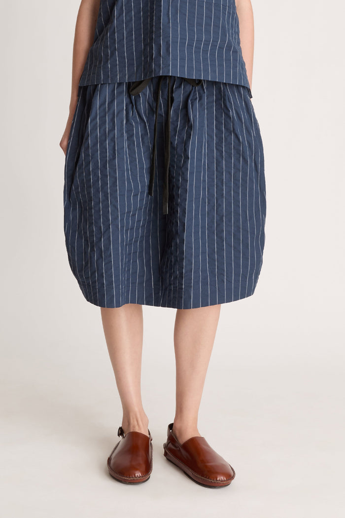 A woman wearing a blue striped top and skirt on a white background