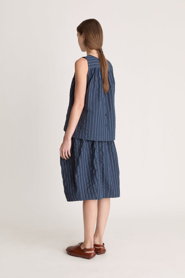 A woman wearing a blue striped top and skirt on a white background