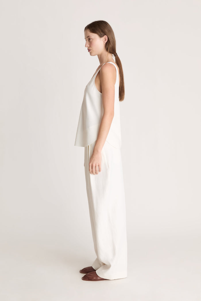 Woman wearing a white tank  top and white trousers on a white background