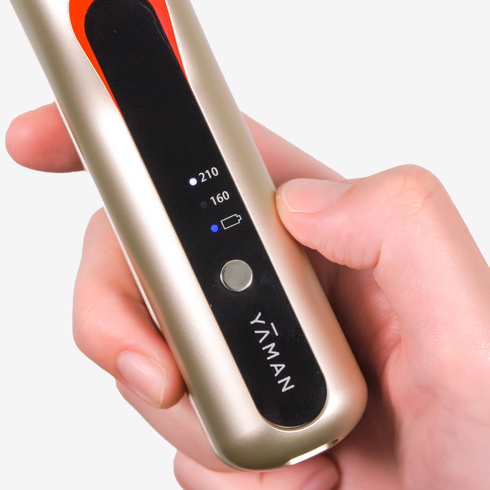 Hand holding a gold and black hair straightener with 'Yáman' branding.