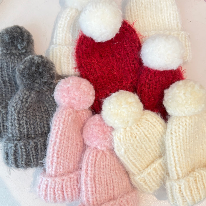 Collection of knitted hats with pom-poms in various colors on a light background