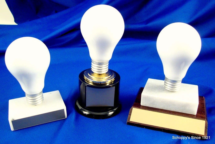 Three light bulb trophies, one on a marble base, one on a black round base, and one atop a slant wood base on marble base