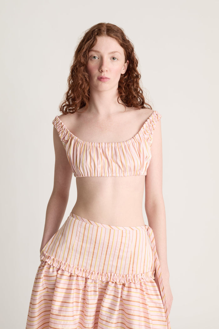 Woman wearing a pink striped crop top and skirt on a plain background