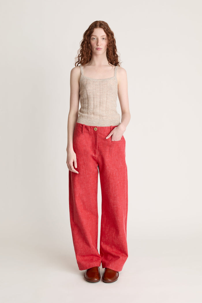 Woman wearing a beige knit cami top and red pants on a white background