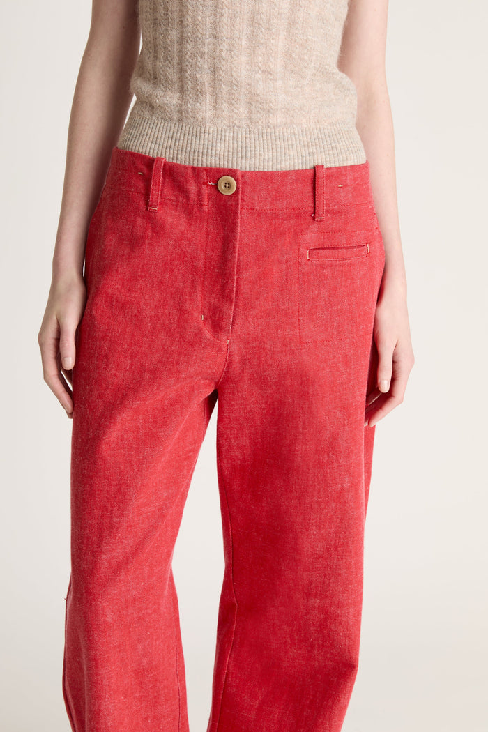 Woman wearing a beige knit cami top and red pants on a white background