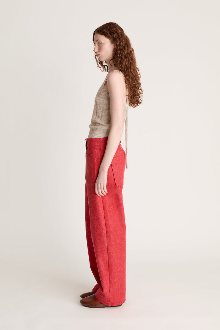 Woman wearing a beige knit cami top and red pants on a white background