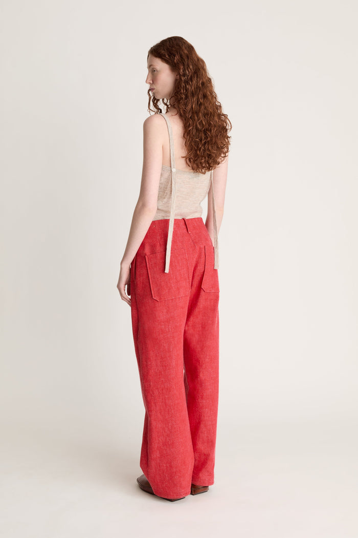Woman wearing a beige knit cami top and red pants on a white background