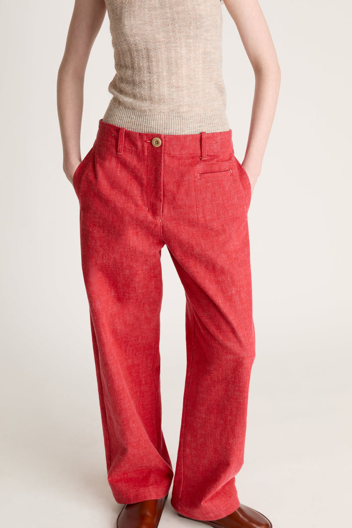 Woman wearing a beige knit cami top and red pants on a white background