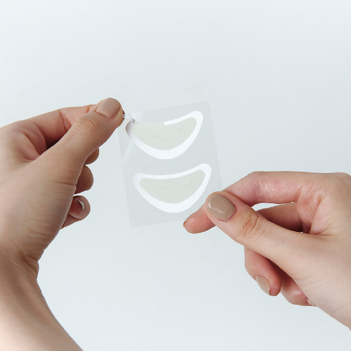 Hands holding a clear sheet with white crescent moon shapes against a light gray background