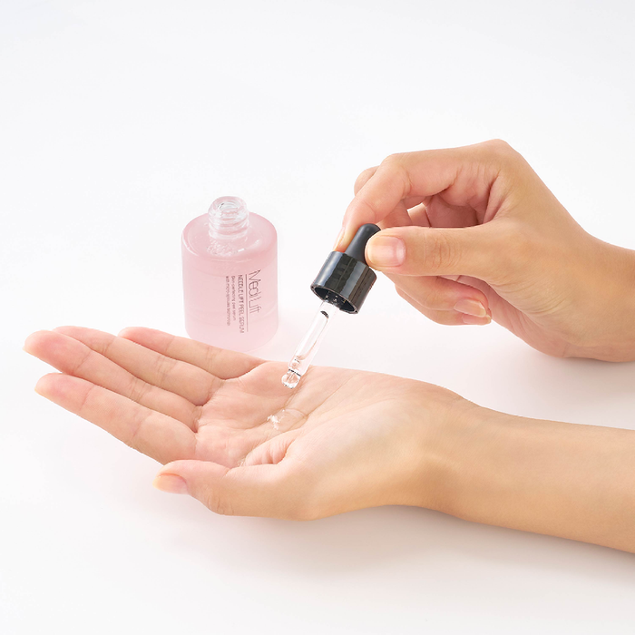 Person holding a dropper with pink liquid over their palm on a white background