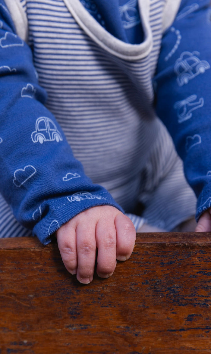 Baby wearing the Deux par Deux organic cotton set with blue transportation-print onesie and striped overalls, view 5