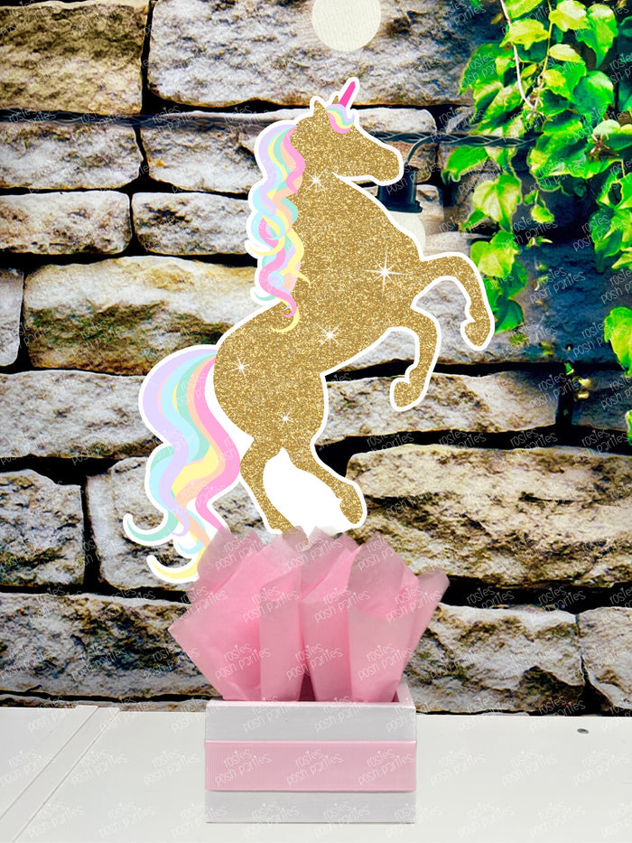 fully decorated unicorn theme table centerpieces for a birthday party or baby shower. Each centerpiece features a cute, pastel color unicorn with printed glitter accents, placed in a white box with colorful tissue paper in shades of blue, purple, mint green, and pink.