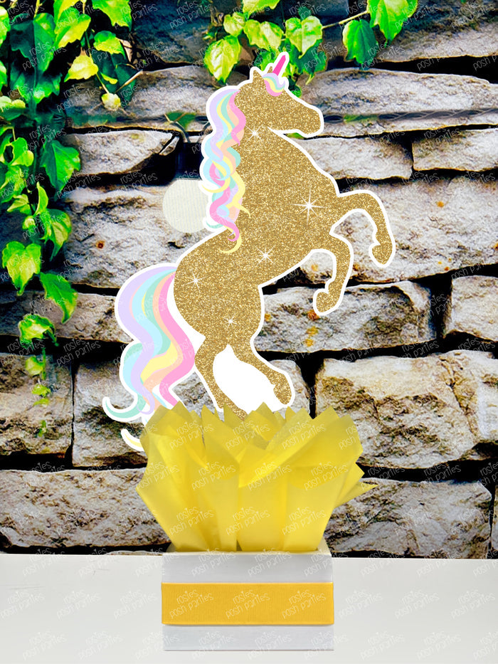 fully decorated unicorn theme table centerpieces for a birthday party or baby shower. Each centerpiece features a cute, pastel color unicorn with printed glitter accents, placed in a white box with colorful tissue paper in shades of blue, purple, mint green, and pink.