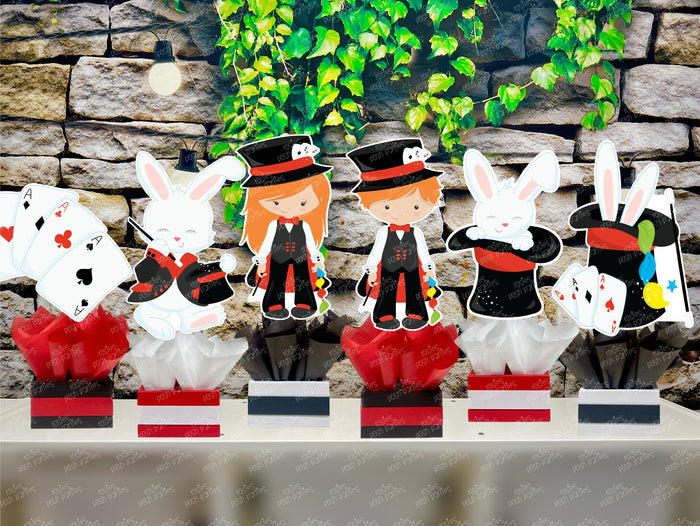 Kids birthday party magician themed centerpieces. The centerpieces feature illustrated cutouts including playing cards, a white rabbit in a tuxedo, a girl magician, a boy magician, a rabbit popping out of a top hat, and a magician's hat with a wand. Each cutout is set in a red, white, or black base filled with matching tissue paper. Receive fully assembled like pictured.