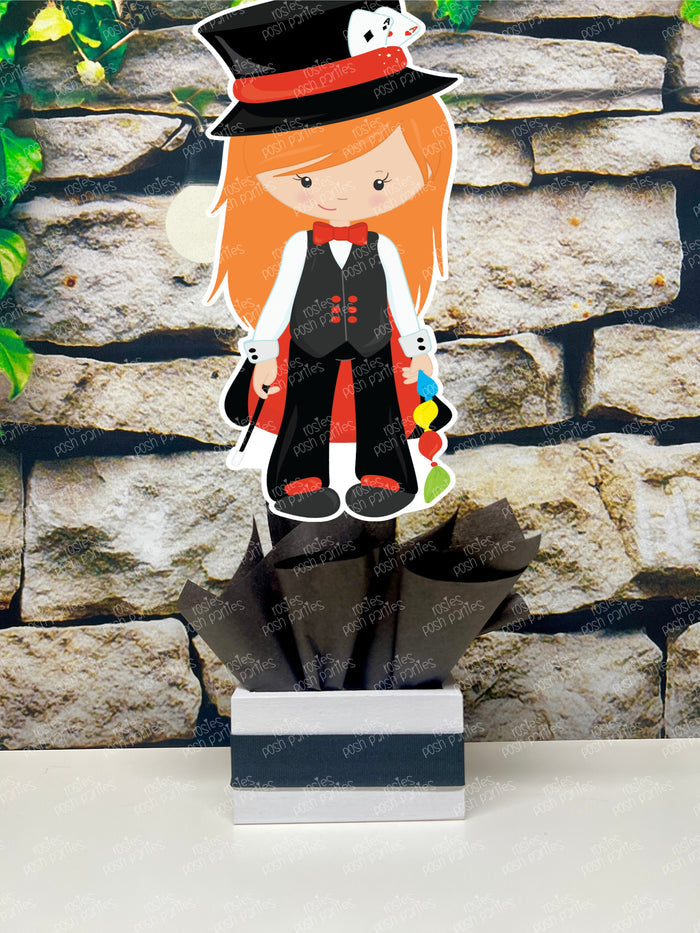 Kids birthday party magician themed centerpieces. The centerpieces feature illustrated cutouts including playing cards, a white rabbit in a tuxedo, a girl magician, a boy magician, a rabbit popping out of a top hat, and a magician's hat with a wand. Each cutout is set in a red, white, or black base filled with matching tissue paper. Receive fully assembled like pictured.