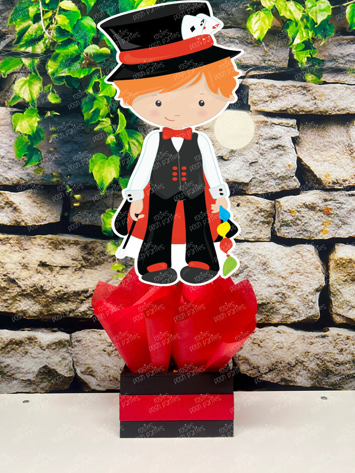 Kids birthday party magician themed centerpieces. The centerpieces feature illustrated cutouts including playing cards, a white rabbit in a tuxedo, a girl magician, a boy magician, a rabbit popping out of a top hat, and a magician's hat with a wand. Each cutout is set in a red, white, or black base filled with matching tissue paper. Receive fully assembled like pictured.