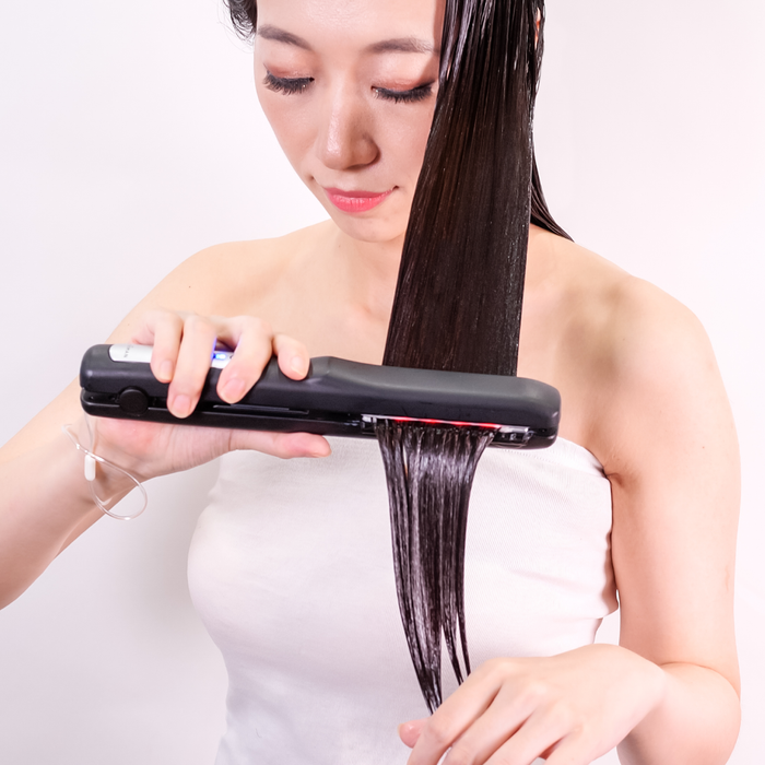 Woman using a hair straightener on her hair against a white background