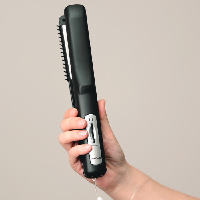 Hand holding a black hair straightener with a visible brand logo on a plain background