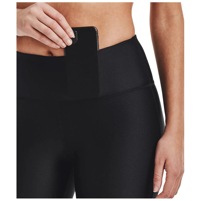 A hand is placing a smartphone into a pocket located on the waistband of black athletic leggings while the background is neutral, emphasizing the activewear and the action of storing the phone.