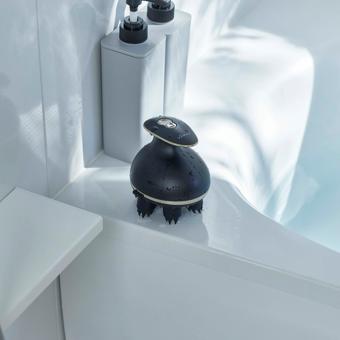 Black handheld shower massager on a white bathtub ledge with a blurred shower head in the background.