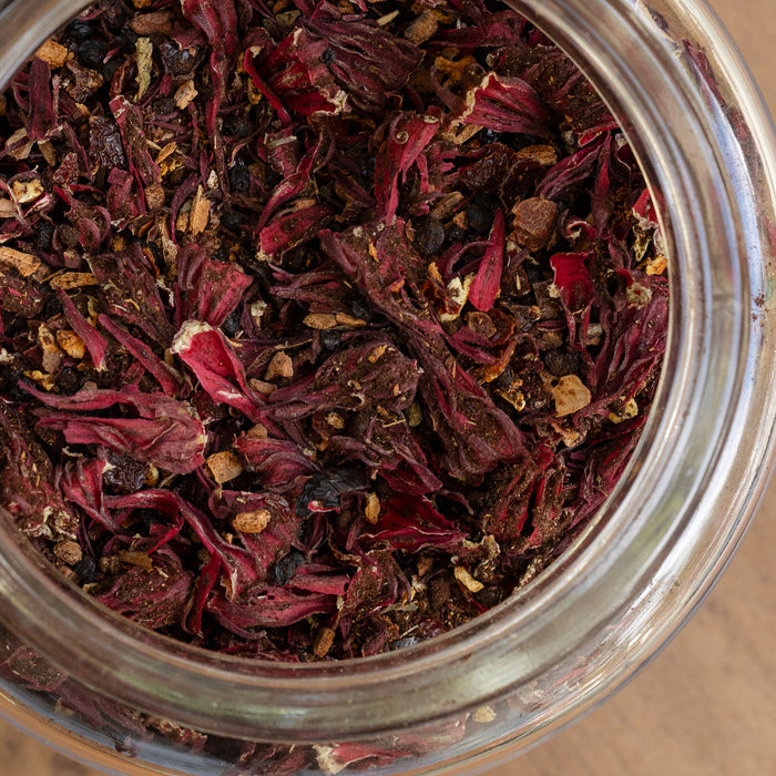 Close-up of a glass jar filled with dried herbs and spices on a wooden surface.